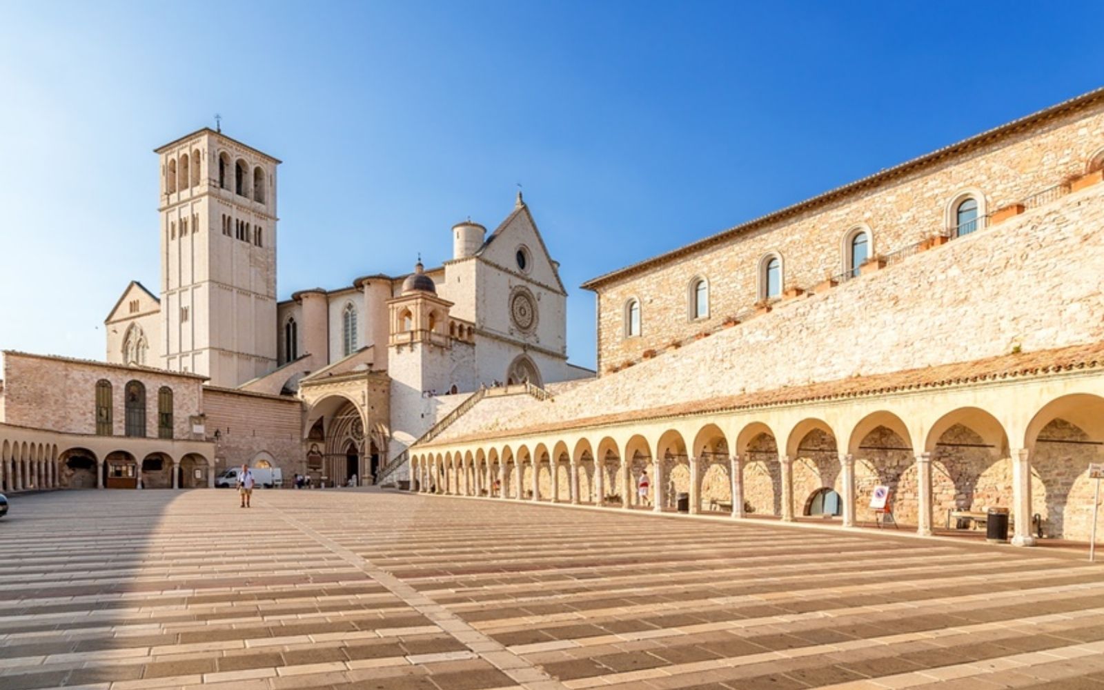 Praça e fachada da Basílica de São Francisco em Assis sob céu azul