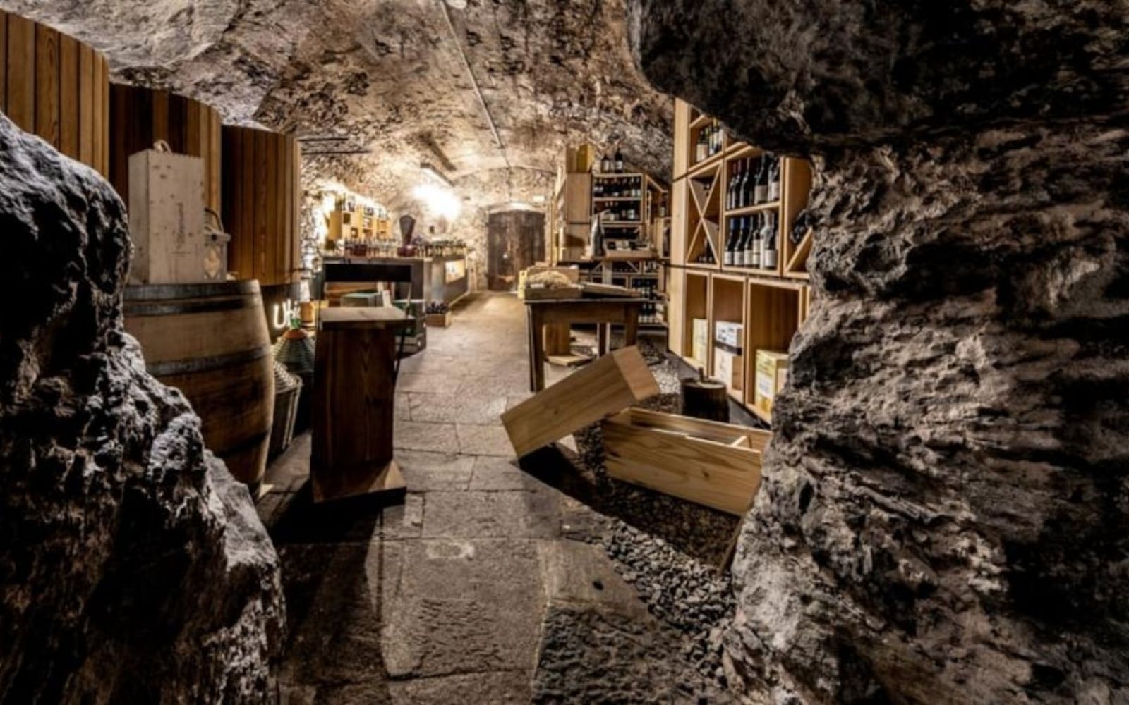 Interior de um crotto com paredes de rocha, barril e prateleiras de vinho