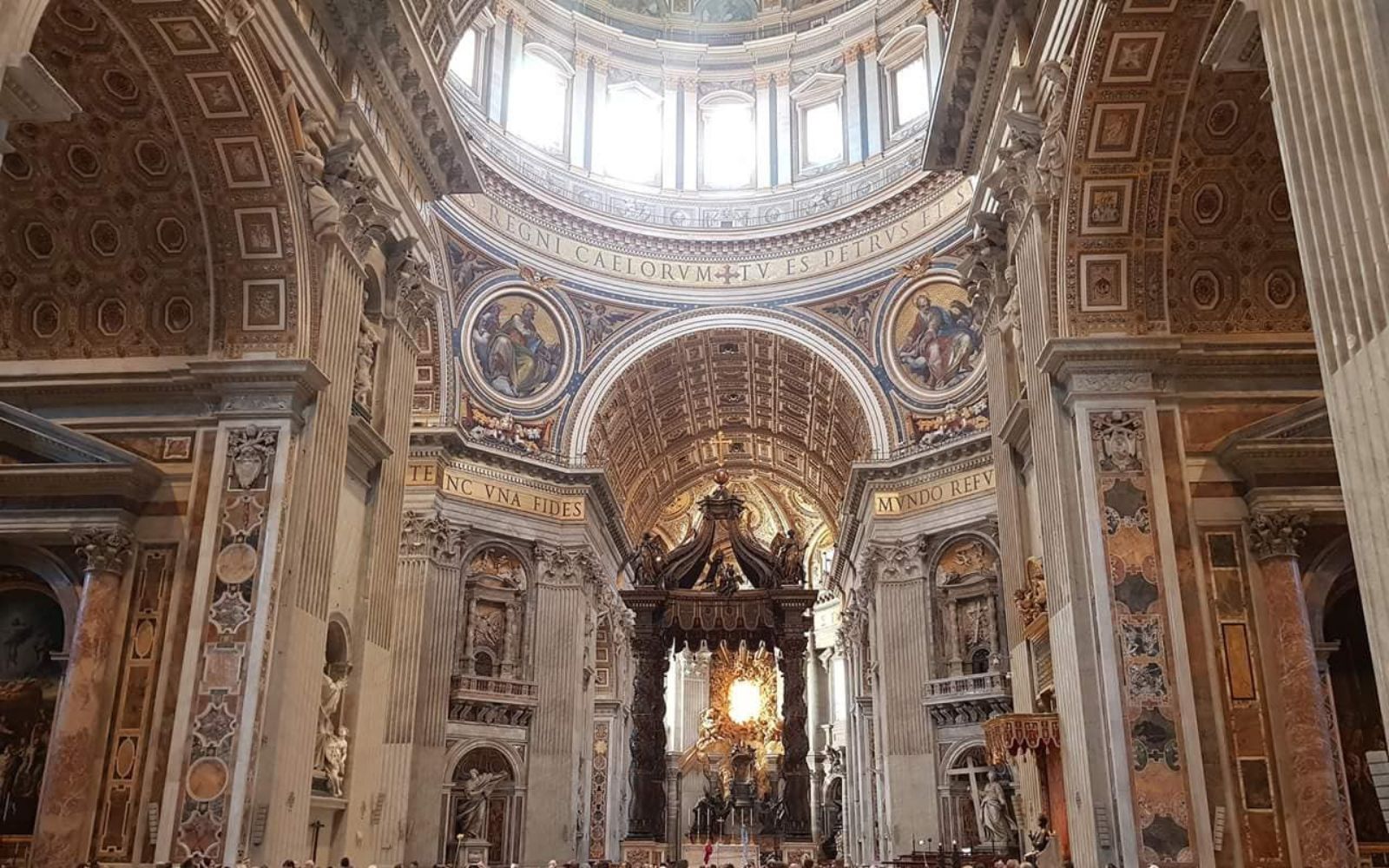 Interior de uma basílica com colunas de mármore, cúpula iluminada e um grande baldaquino