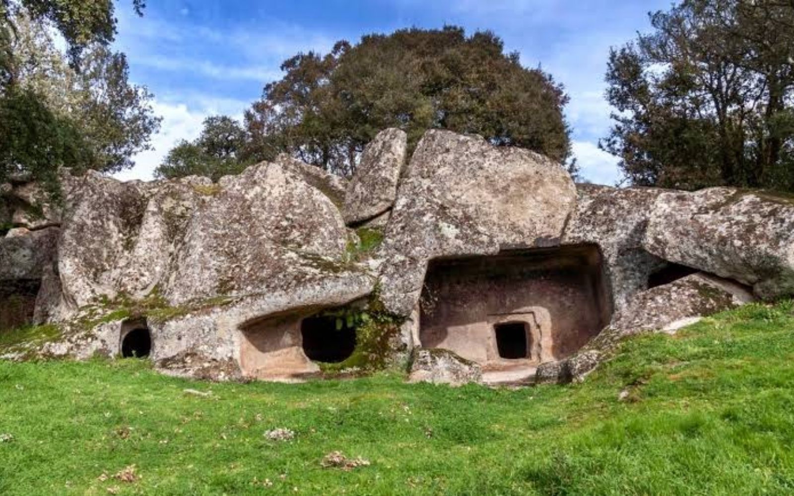 Entradas de Domus de Janas escavadas em grandes blocos de rocha cercados por árvores