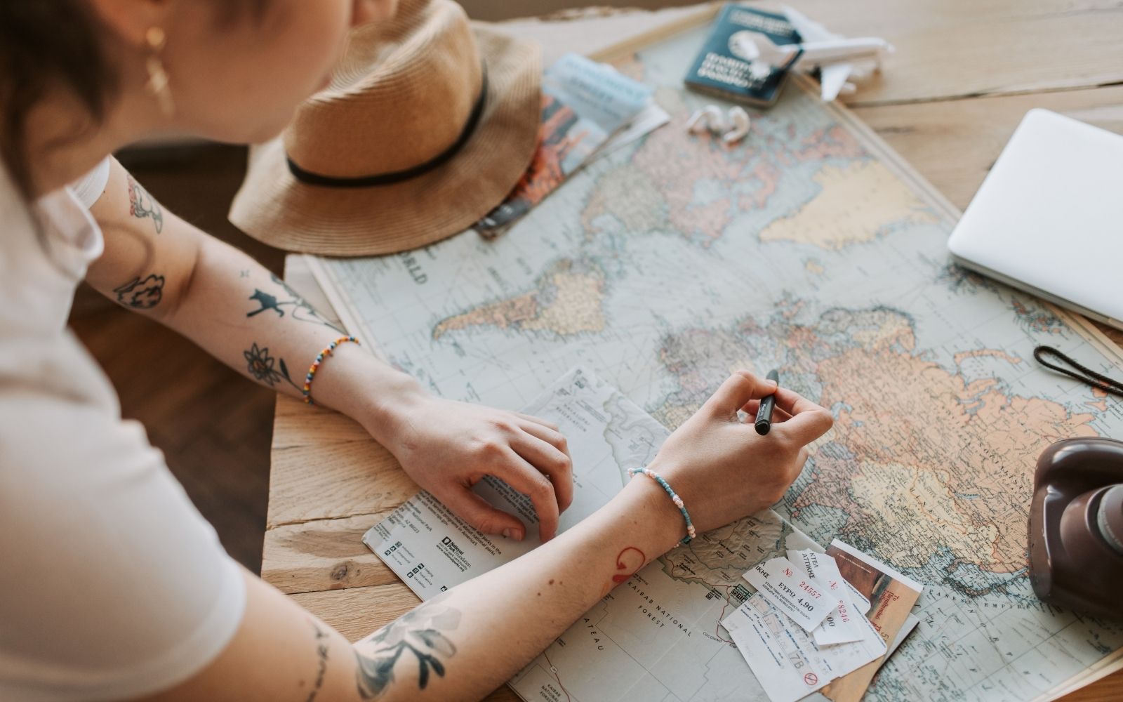 Pessoa planejando uma viagem sobre um mapa com passagens e chap&eacute;u