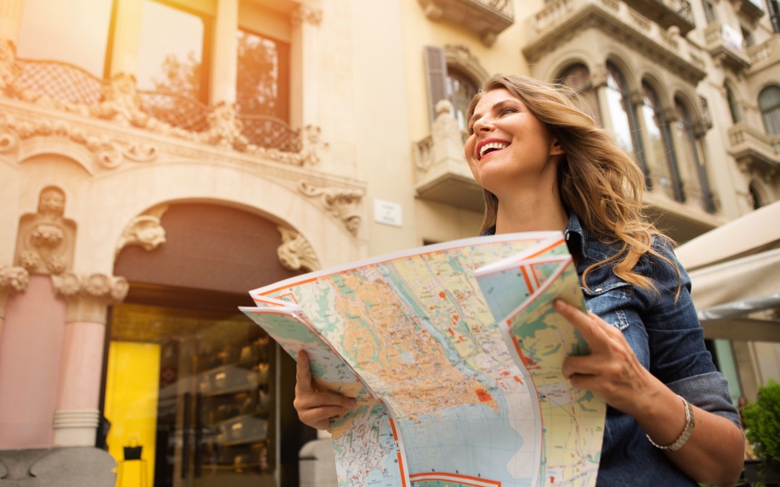 Mulher sorrindo com um mapa nas m&atilde;os em uma rua europeia