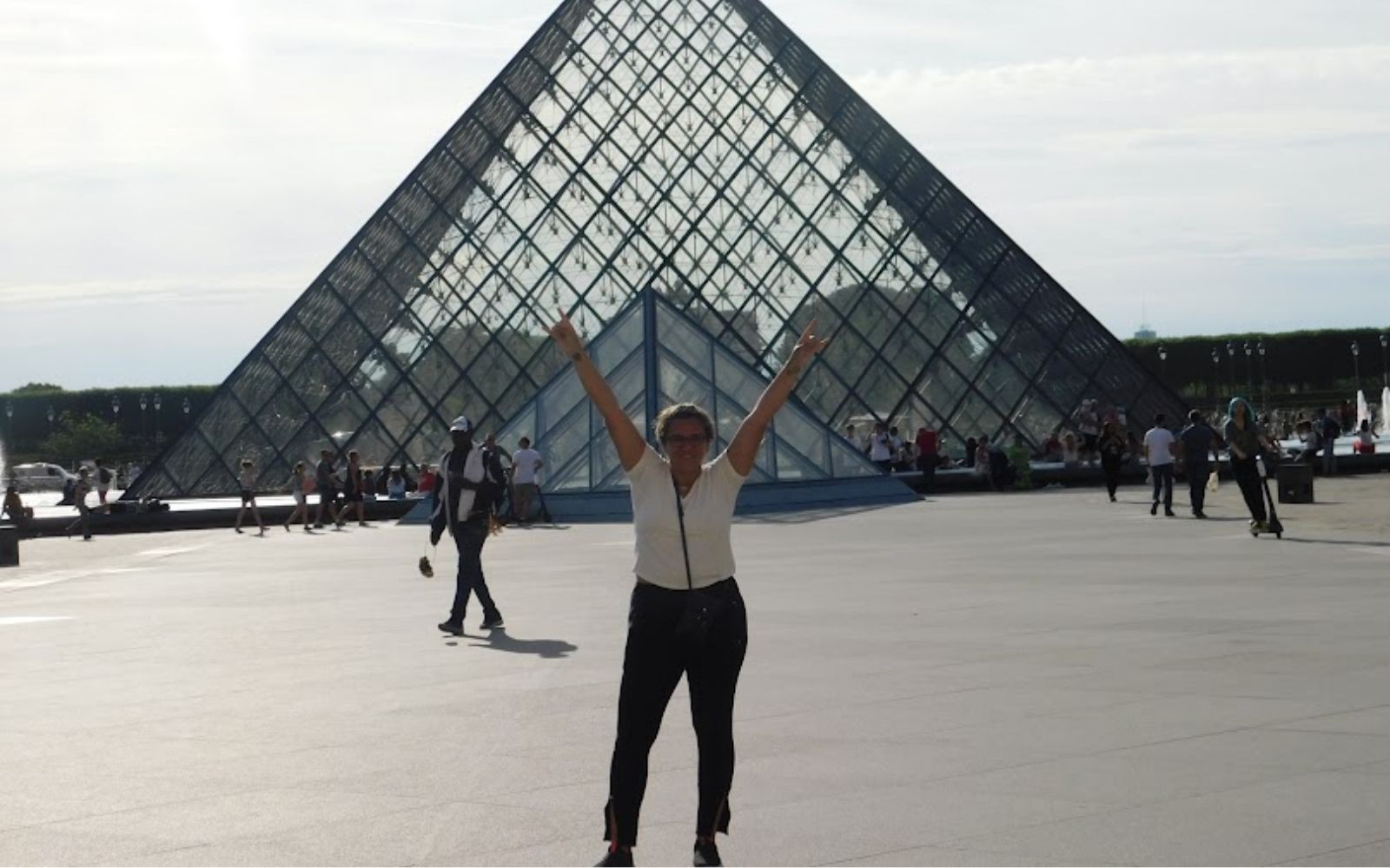 Mulher em frente &agrave; pir&acirc;mide do Louvre durante uma viagem sozinha