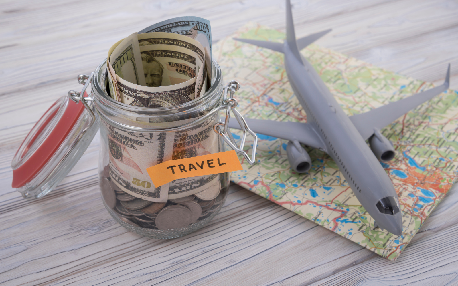 Pote com dinheiro para viagem, mapa e miniatura de avião sobre uma mesa